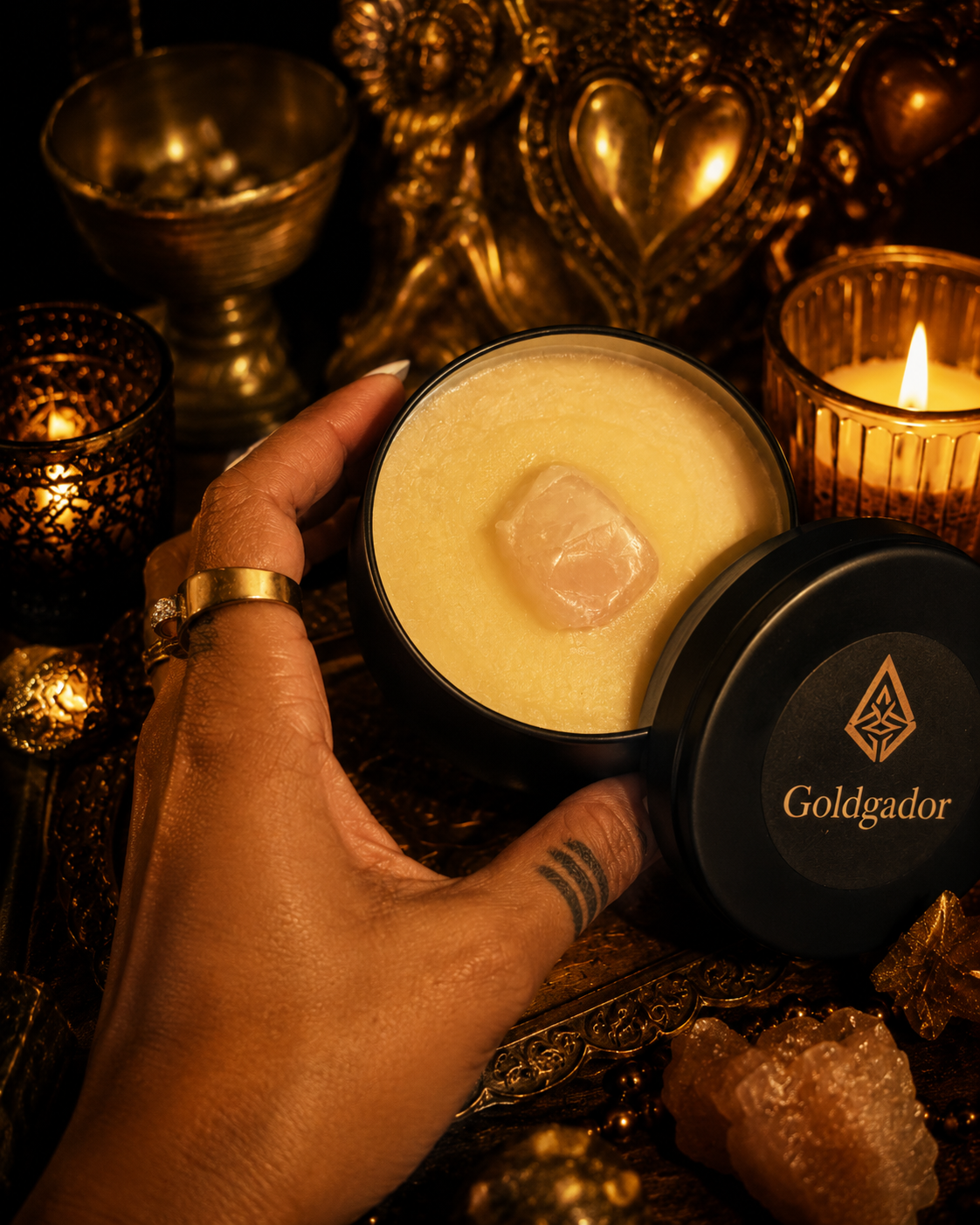 Goldgador Black — a potent black-tin body butter, golden seal placed at the centre, held in the practitioner's hand by candlelight